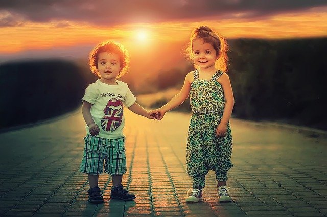 niño y niña cogidos de la mano con el sol detrás en atardecer